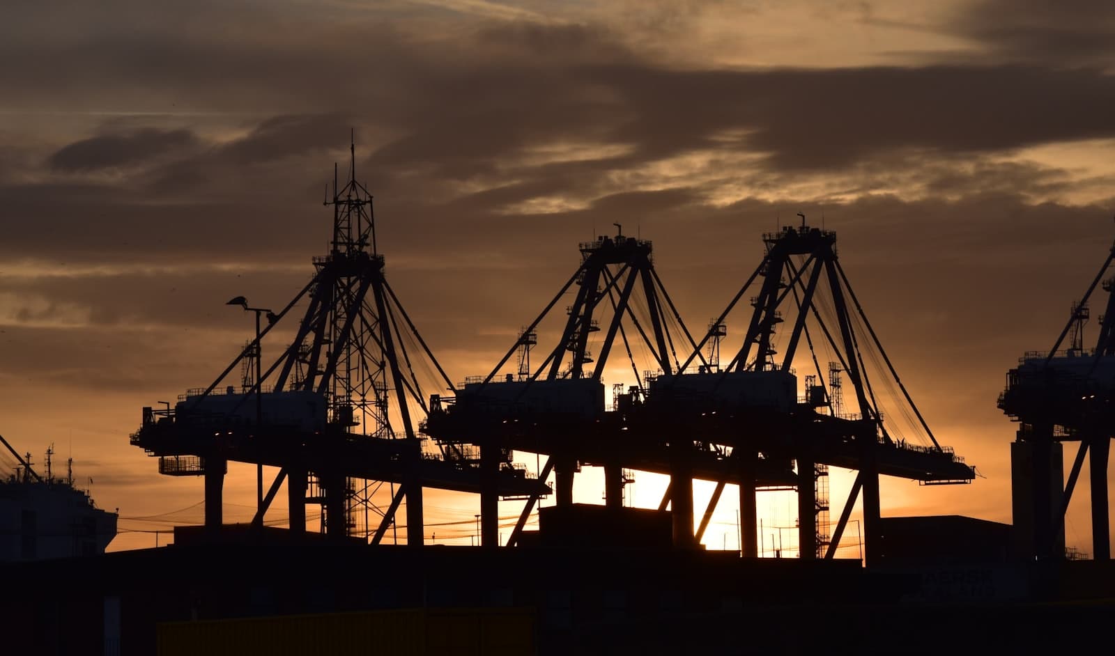 Grúas de contenedores en el puerto recortadas contra un cielo dorado al atardecer